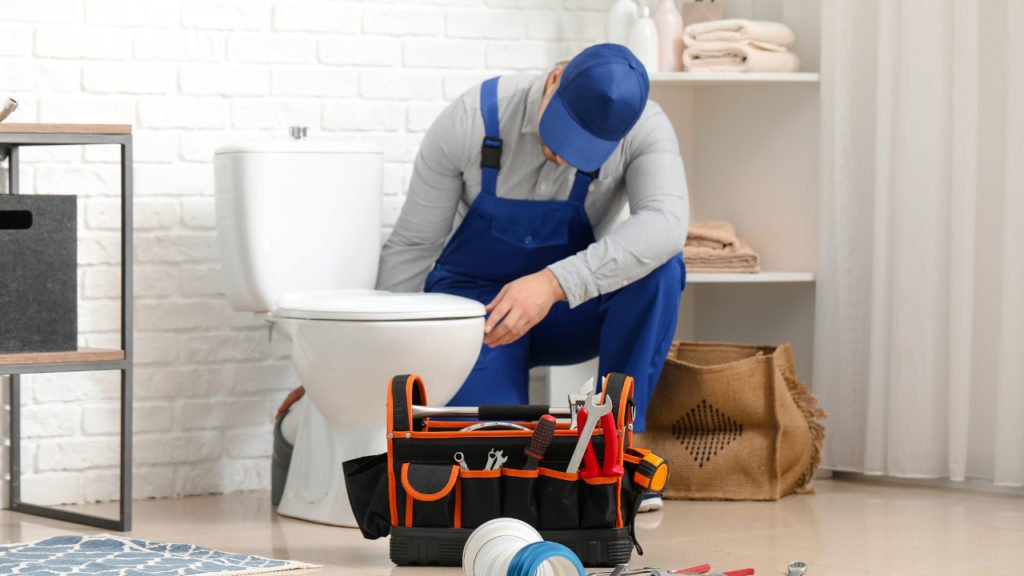 A man wearing a plumber uniform with a tools repairing a toilet bowl